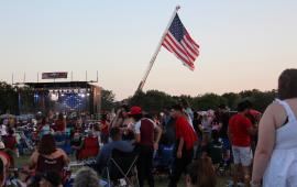 Image of crowd in front of stage at 4th of July with large US flag in background
