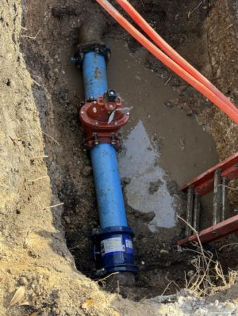 picture of an exposed water line with valve in a dug out hole with a ladder alongside wall of muddy dirt