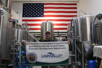 Owner of Longtab Brewing is holding a large check in front of the new tank