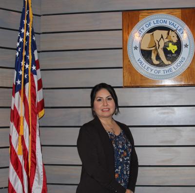 picture of Lisa Hernandez next to American flag and City Seal plaque